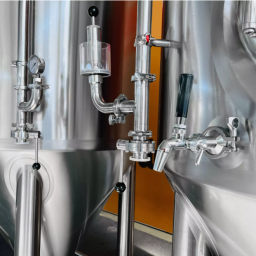 Shiny stainless steel brewing tanks with valves and pipes.